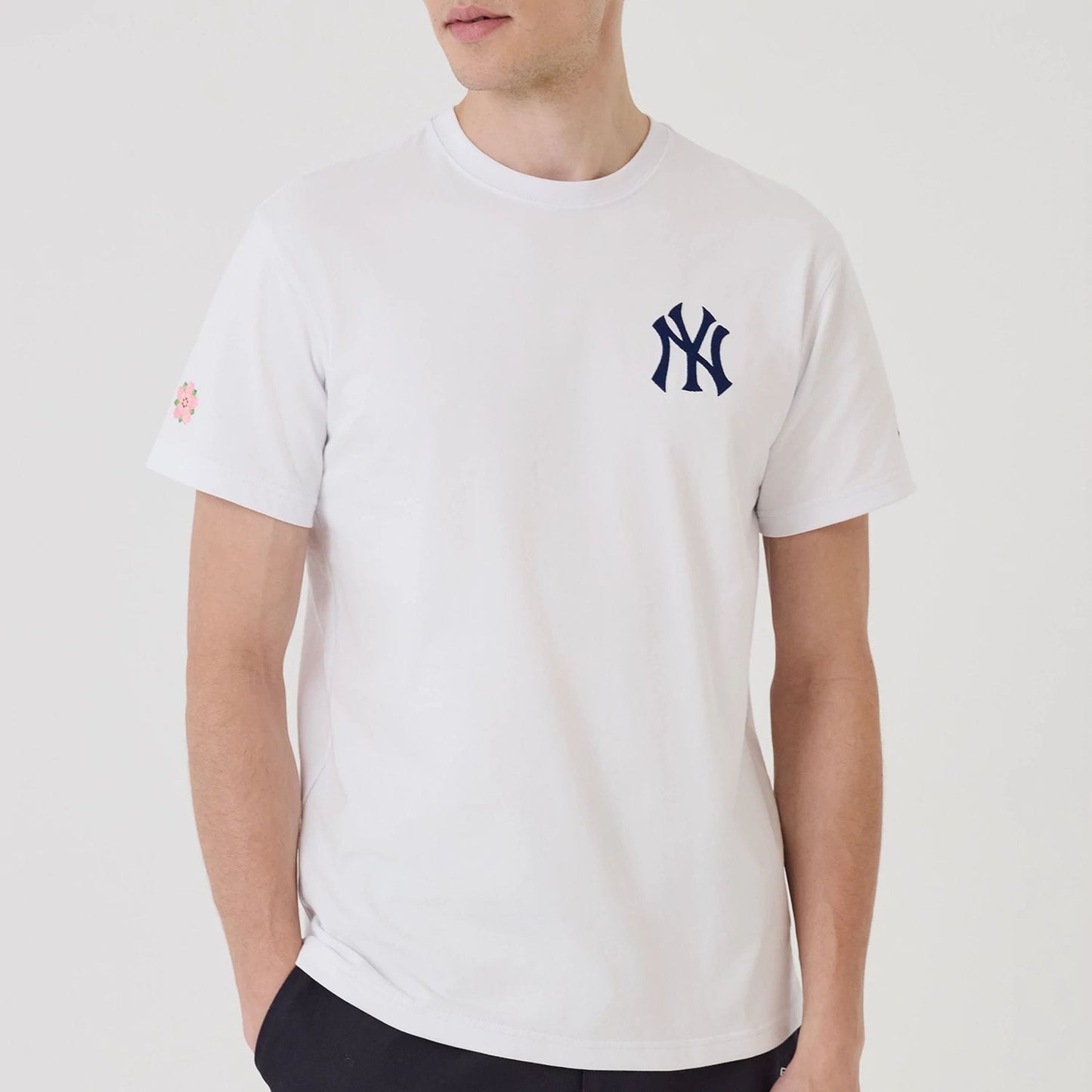 New York Yankees MLB Sakura White T-Shirt, front view showing a navy NY logo on the left chest and a small pink sakura flower icon on the left sleeve against a plain white fabric background.