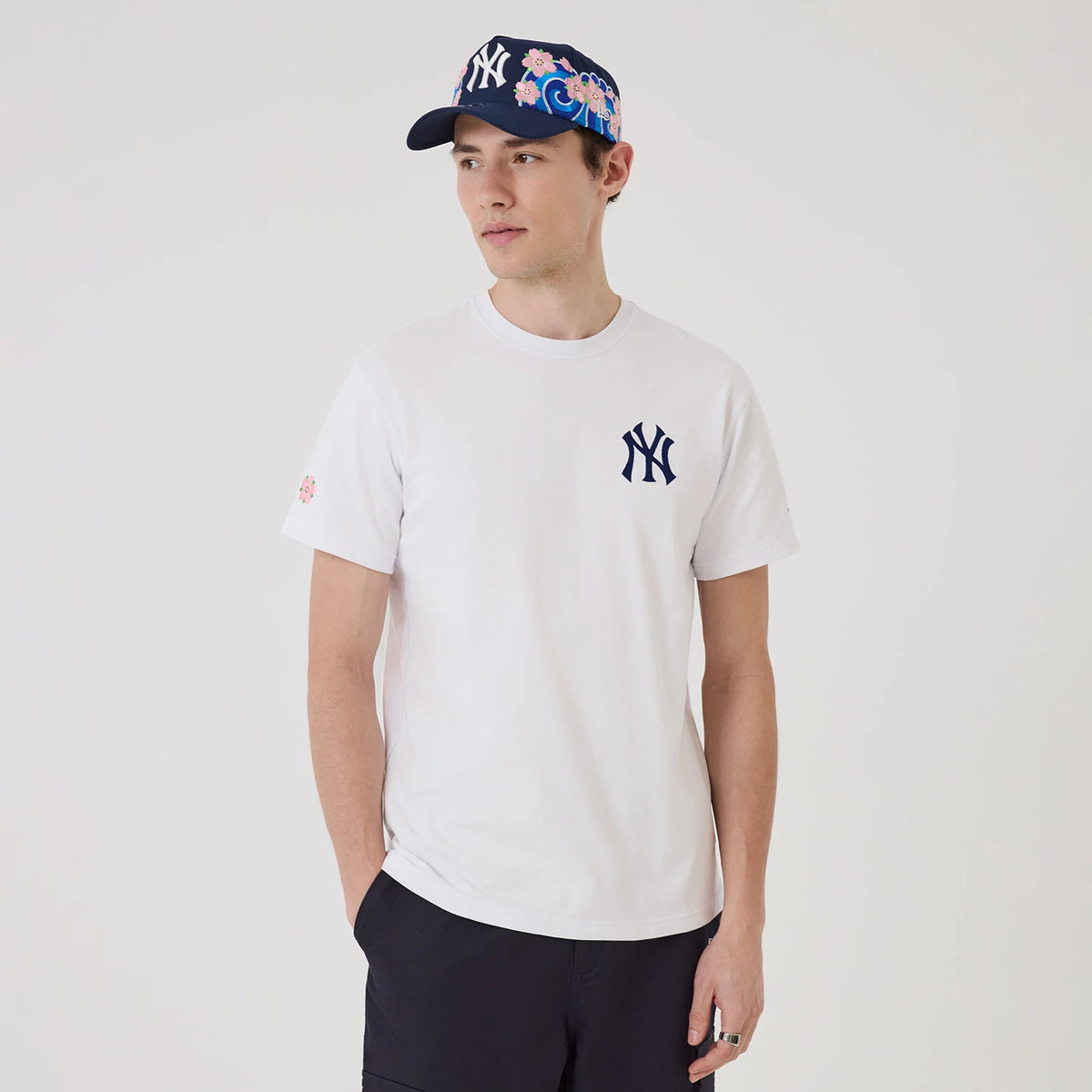 New York Yankees MLB Sakura White T-Shirt, on-model view showing navy NY logo on left chest, cherry blossom detail on right sleeve, paired with a navy cap featuring a raised NY logo and pink cherry blossom pattern over the crown.