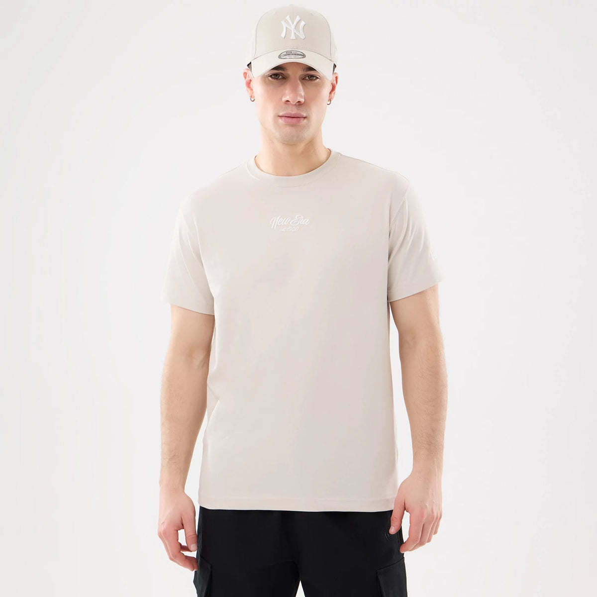 New Era Resort Natural T-Shirt, front view showing the natural-coloured tee with a raised New Era logo centred on the chest, short sleeves, and a man wearing a matching cap with a raised white NY logo on the front.