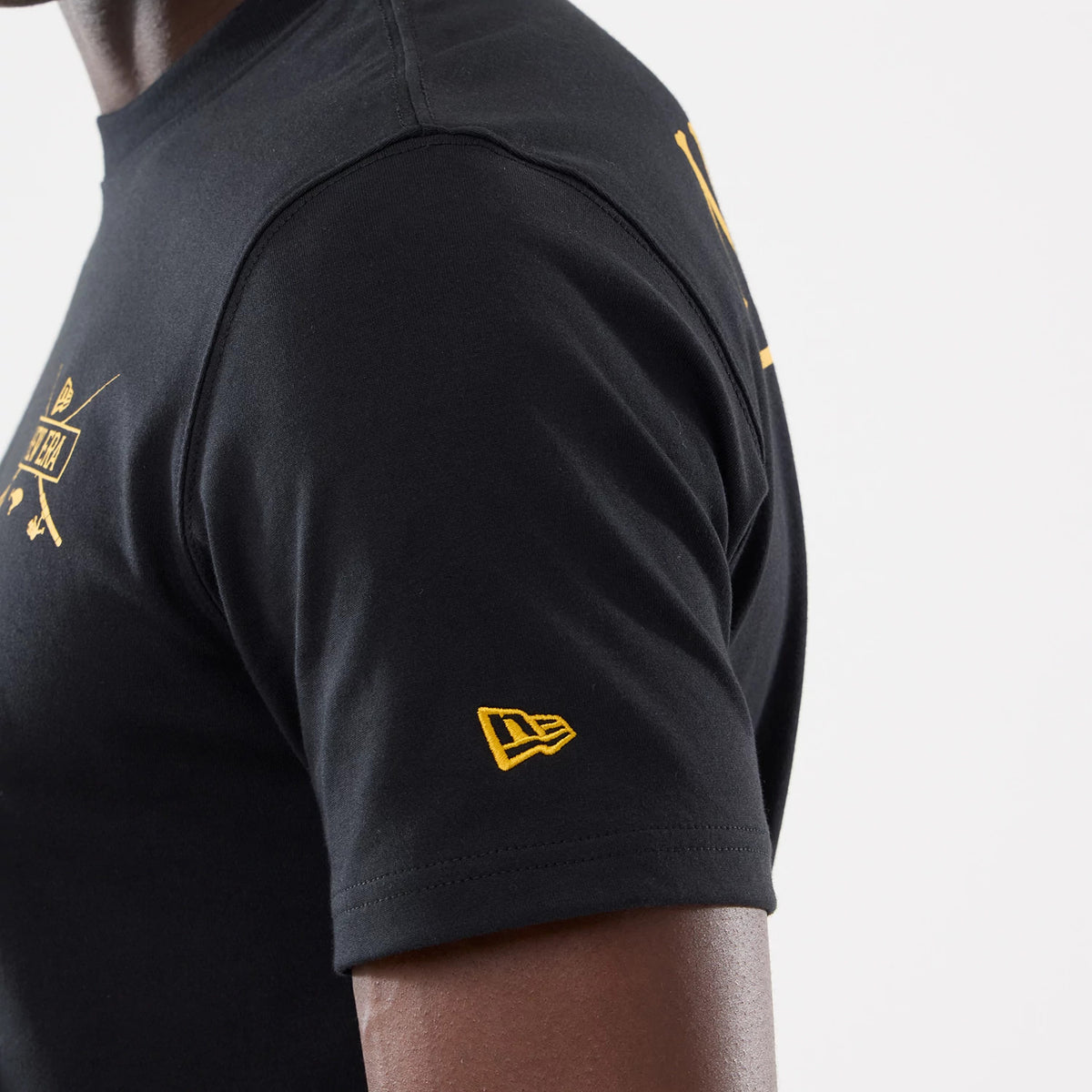 New Era Graphic Outdoor Fishing Black T-Shirt, side view showing a black sleeve with a raised yellow New Era logo near the hem and part of a yellow graphic across the chest area on the black fabric.