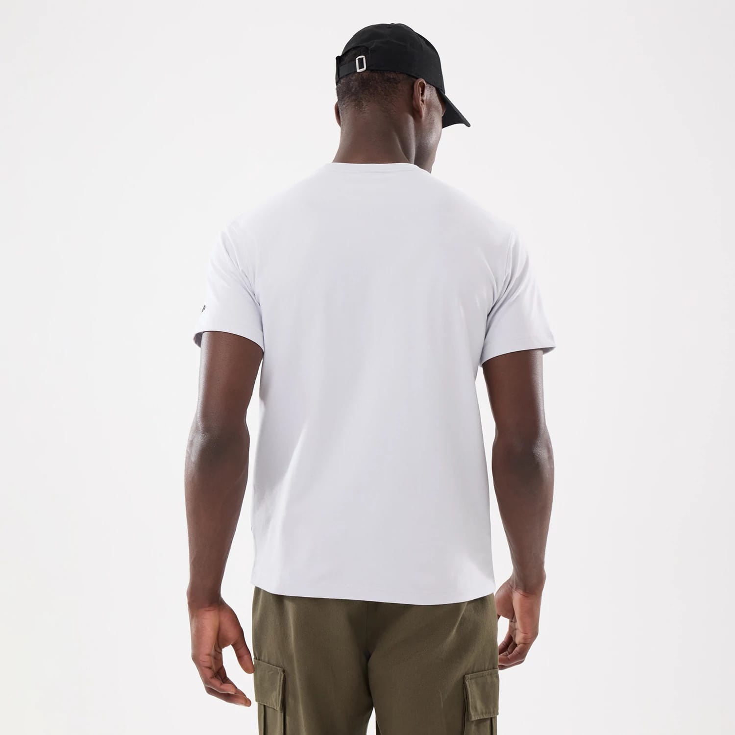 New Era Basic White T-Shirt, rear view showing the plain white back of the t-shirt with short sleeves, a small debossed New Era logo on the left sleeve, and a person wearing a black cap.