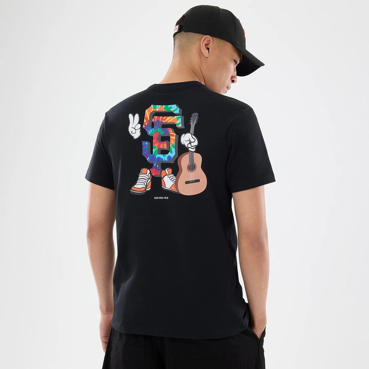 San Francisco Giants MLB Cartoon Black T-Shirt, on-model view showing the vibrant cartoon-style graphic on the back featuring the number six in multicolour with arms and legs, holding a guitar and making a peace sign, on a black shirt.