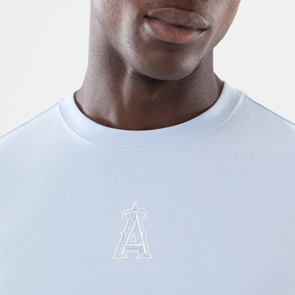 New Era LA Angels MLB Cartoon Blue T-Shirt, front view featuring a light blue shirt with a raised white logo centred on the chest, showing an angelic 'A' with a halo, worn by a model.