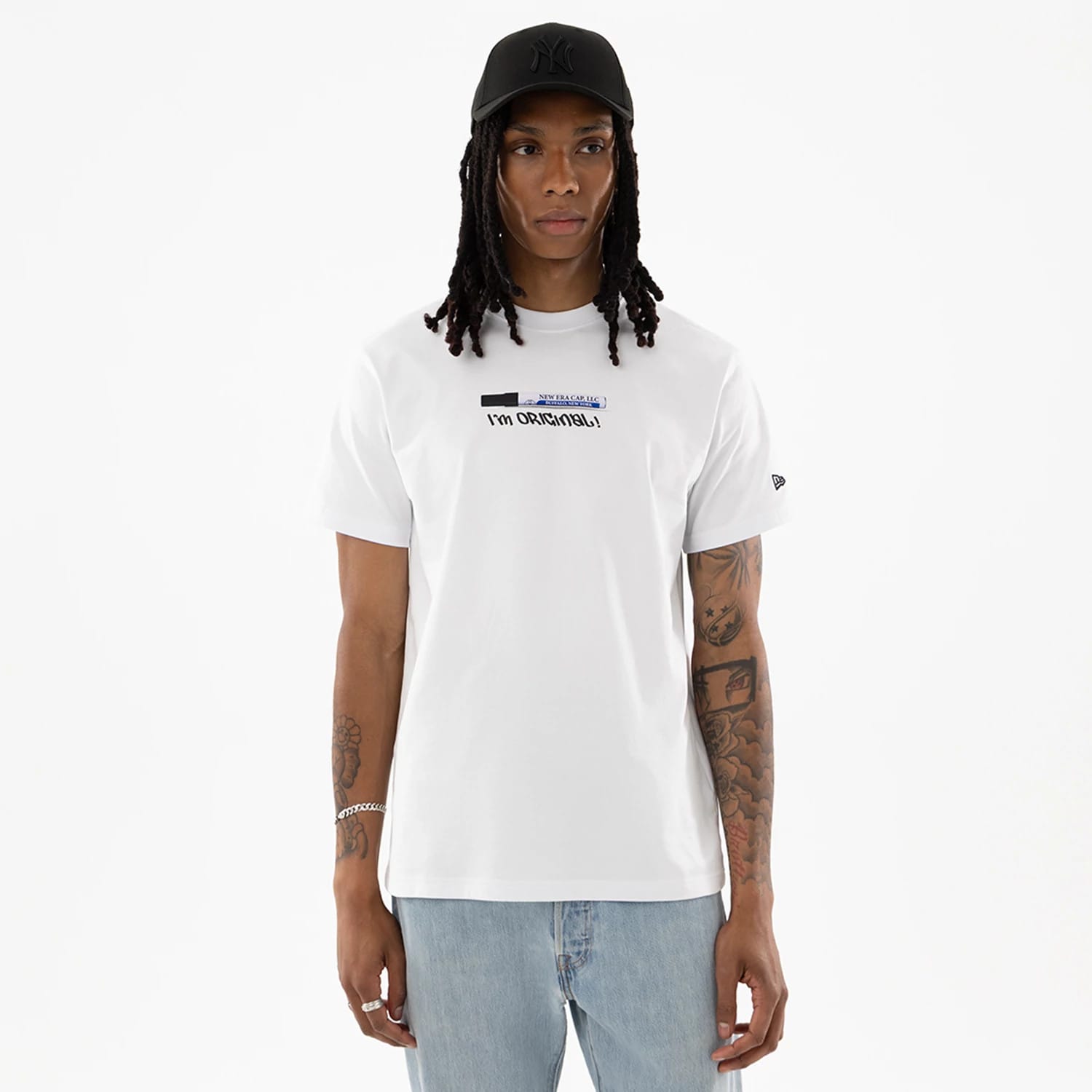 New Era I Am Original White T-Shirt, on-model view showing a white T-shirt with "I’m ORIGINAL" text design on the chest, a debossed logo on the left sleeve, paired with light blue jeans and a black cap with a raised logo.