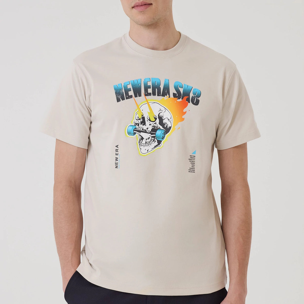 New Era SK8 Graphic Cream T-Shirt, front view showing a bold graphic of a skull with skate wheels as eyes on the chest, vibrant colours including orange and blue, and the debossed New Era logo vertically printed on the left side.