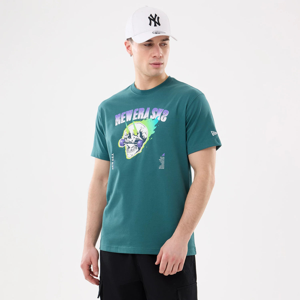 New Era SK8 Graphic Dark Green T-Shirt, on-model view showing a graphic skull design with text across the chest, a small raised New Era logo on the left sleeve, and the model wearing a white cap with a black logo.