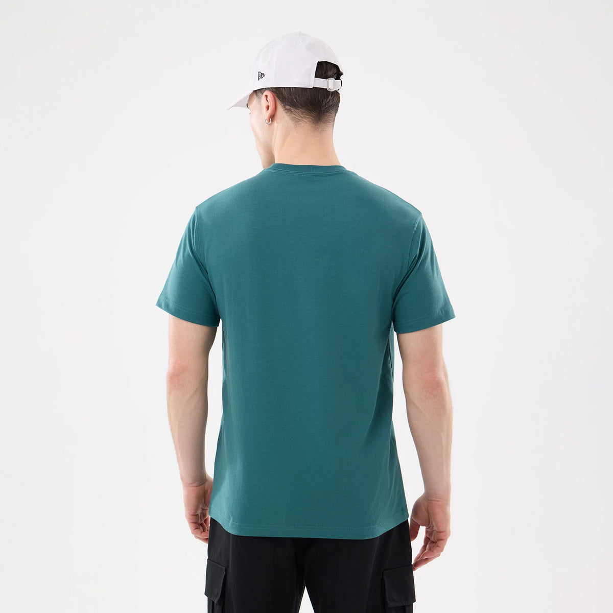 New Era SK8 Graphic Dark Green T-Shirt, on-model view showing the back of a dark green T-shirt with short sleeves and a crew neckline, worn by a person in black cargo trousers and a white cap with a debossed logo.