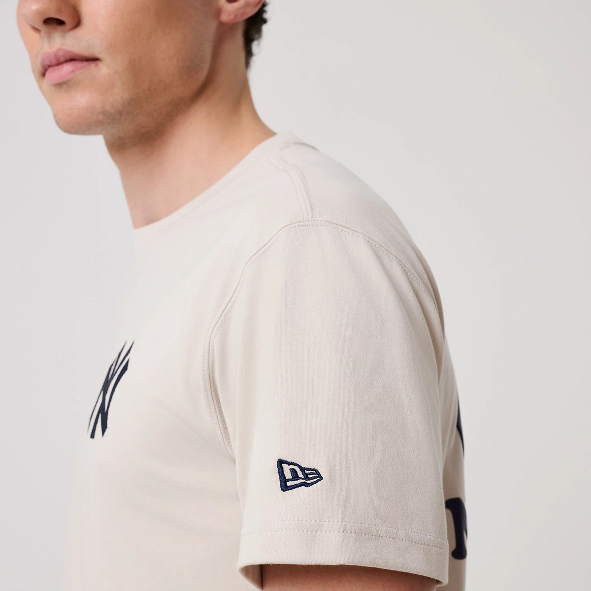 New York Yankees MLB Banana Graphic Natural T-Shirt, side view showing the natural colour fabric with a raised New Era logo embroidered near the bottom of the sleeve and the Yankees logo visible on the chest.