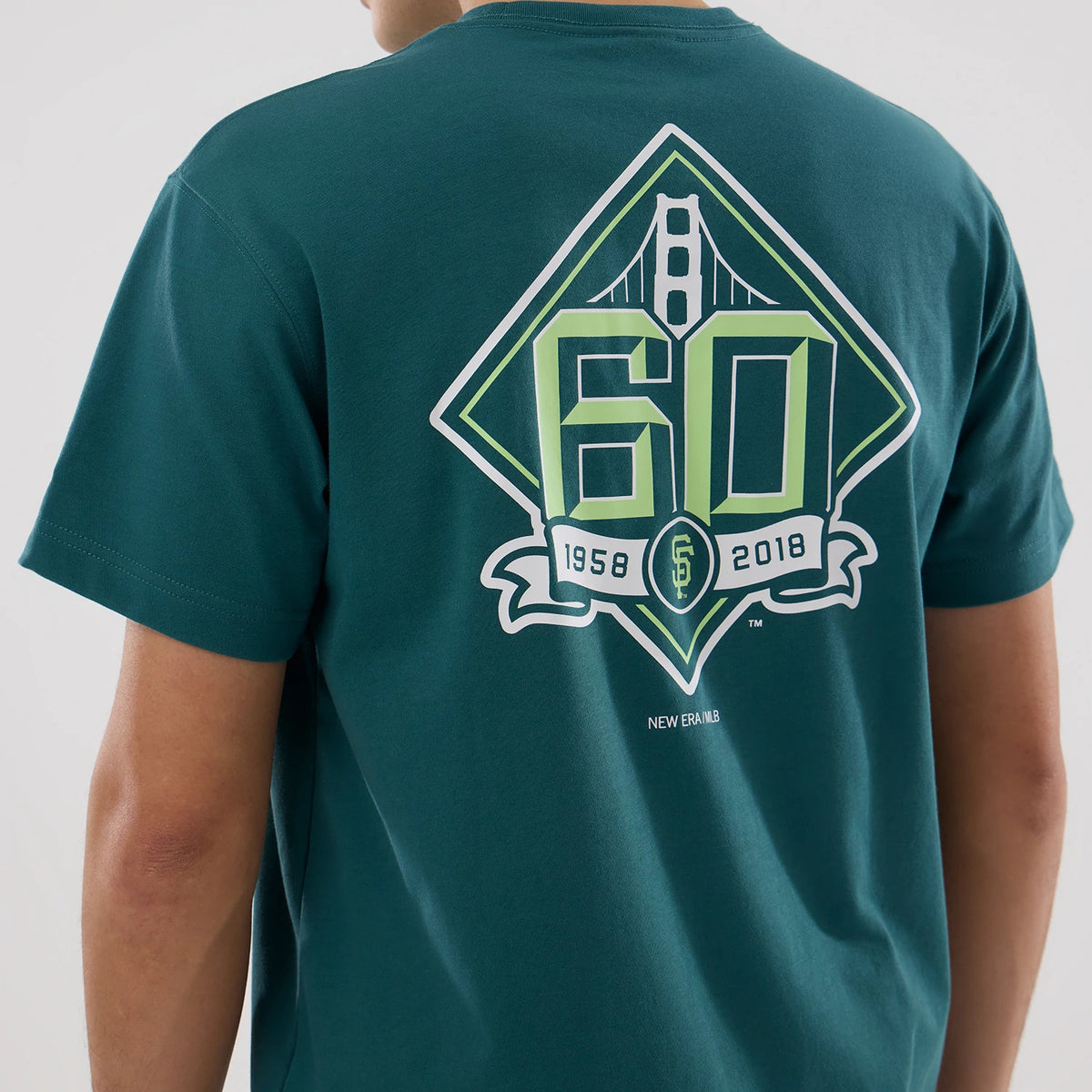 San Francisco Giants MLB Garden Dark Green T-Shirt, rear view showing a large graphic design featuring '60' and '1958-2018' in green and white beside the Golden Gate Bridge on the dark green fabric with a small New Era logo below.
