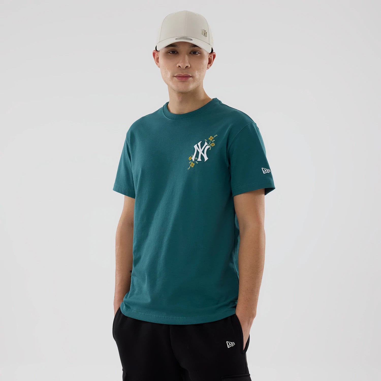 New York Yankees MLB Garden Dark Green T-Shirt, on-model view showing a green shirt with a white NY logo with floral design on the chest and a white New Era logo on the left sleeve, styled with a cream cap featuring a debossed logo.