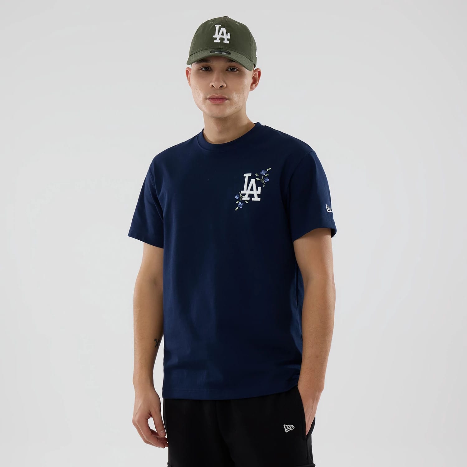 LA Dodgers MLB Garden Blue T-Shirt, on-model view showing the LA logo with floral accents on the navy front, a small New Era logo on the left sleeve, paired with an olive cap featuring a raised LA logo.