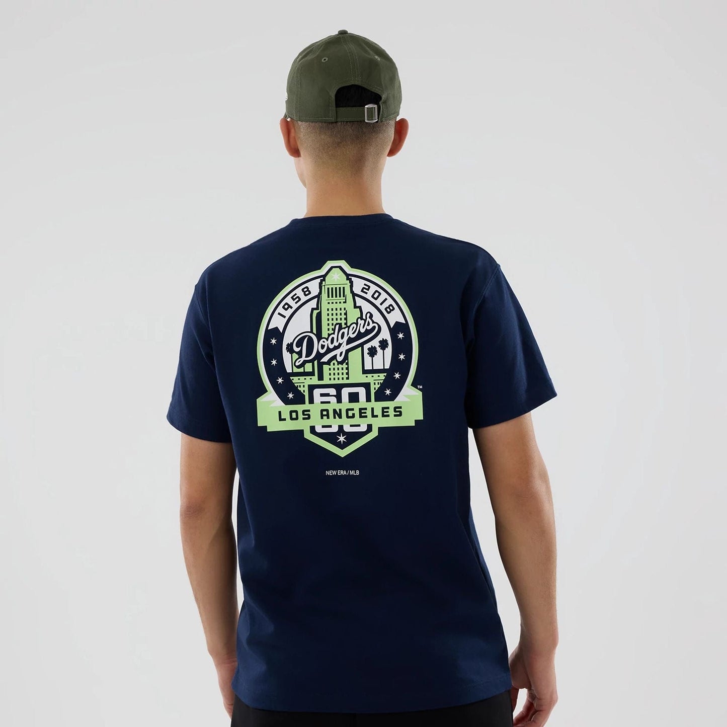 LA Dodgers MLB Garden Blue T-Shirt, rear view showing a large green Dodgers and Los Angeles graphic centred on the back, worn by a person in a green cap with a metal buckle and eyelets.
