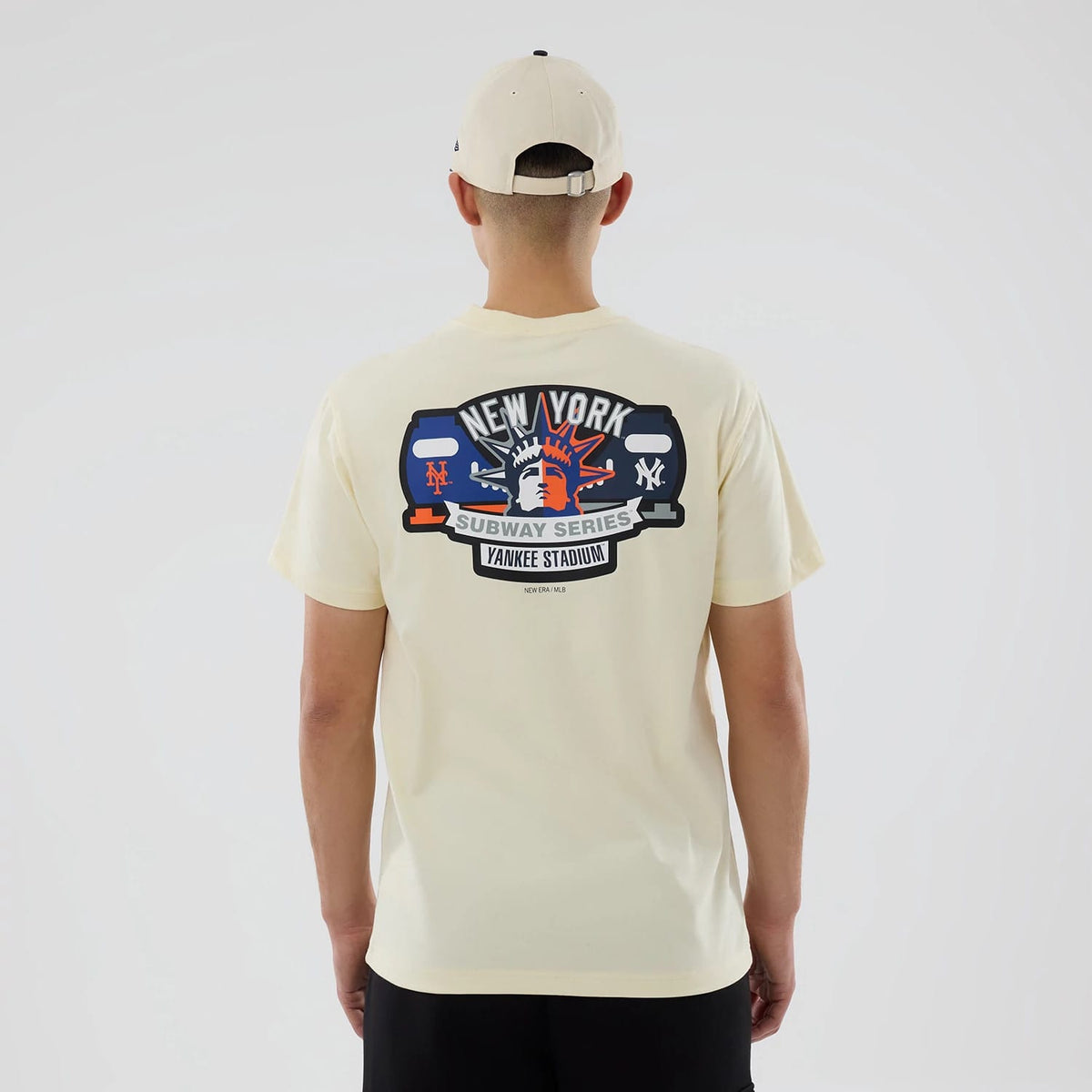 New York Yankees MLB City Series Cream T-Shirt, rear view showing a large colourful graphic of the Statue of Liberty with "New York Subway Series Yankee Stadium" text in black and blue on the upper back, worn by a person.