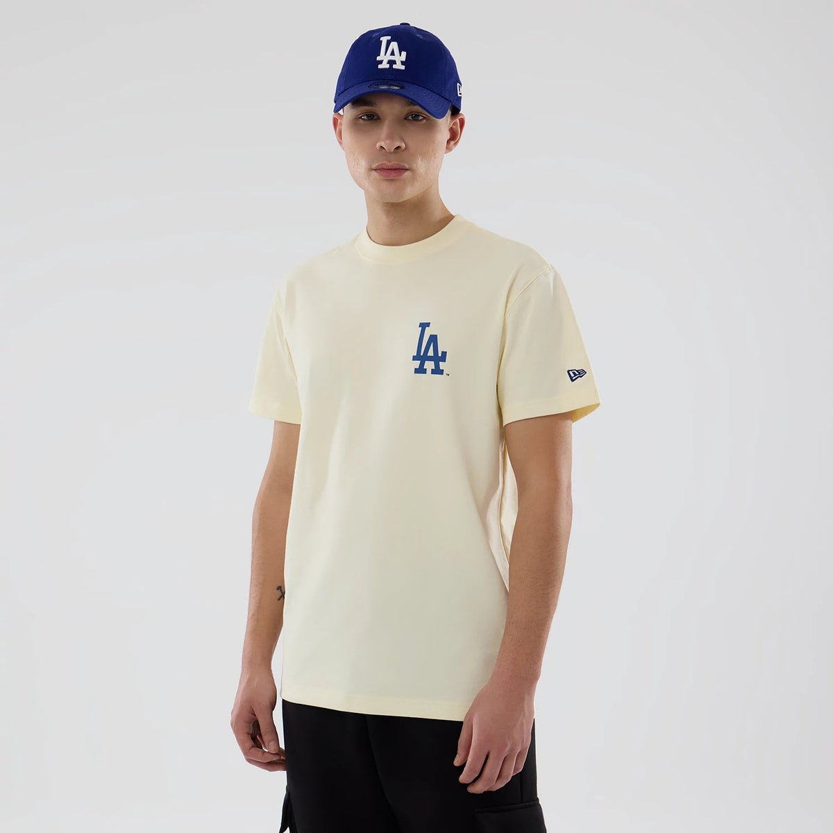 LA Dodgers MLB City Series Cream T-Shirt, on-model view showing a cream T-shirt with a blue LA logo on the chest, a New Era logo on the left sleeve, paired with a blue cap featuring an LA logo.