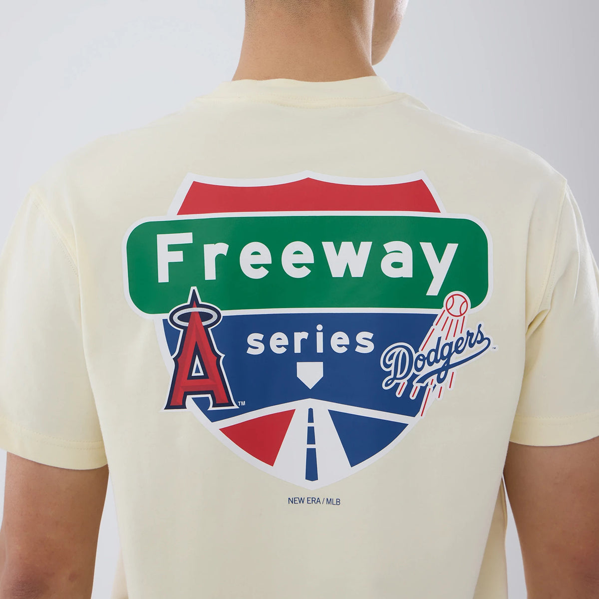 LA Dodgers MLB City Series Cream T-Shirt, rear view showing a large freeway-inspired graphic with a red, green, and blue sign design featuring the Dodgers logo on cream fabric and the New Era/MLB logo printed below.