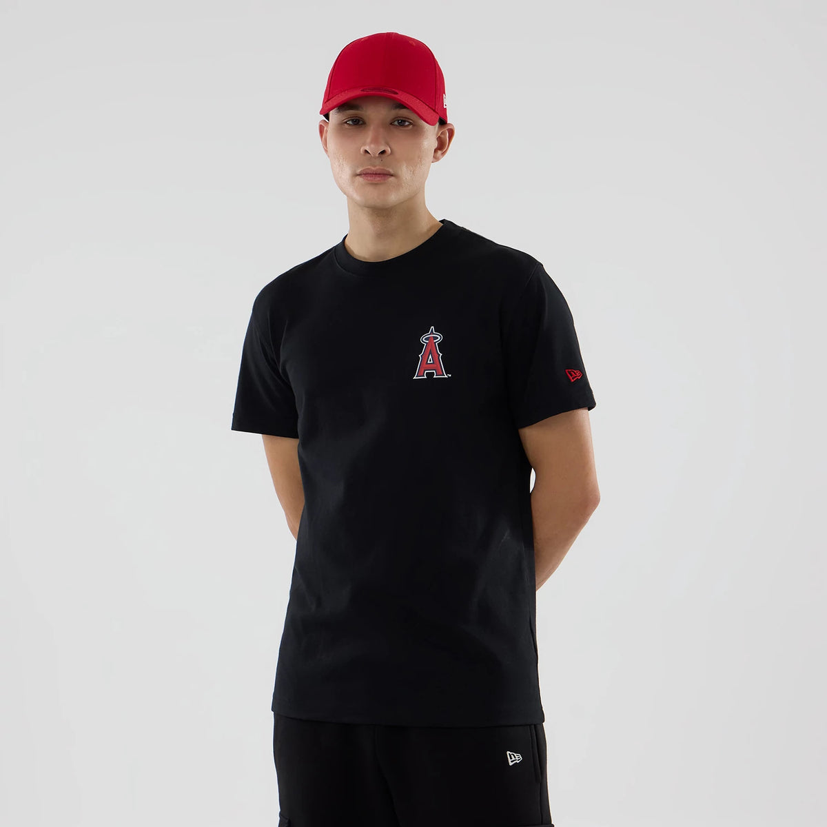 LA Angels MLB City Series Black T-Shirt, front view showing the red and white LA Angels logo printed on the left chest, a person wearing a red cap with a raised logo on the side, and an embroidered red New Era logo on the sleeve.