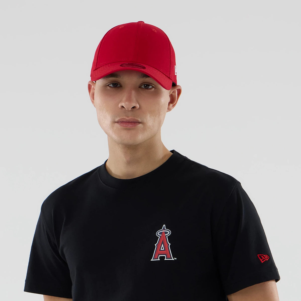 LA Angels MLB City Series Black T-Shirt, on-model view showing the red embroidered Angels logo on the left chest, a red cap with a debossed logo worn by the model, and the red embroidered New Era logo on the sleeve.