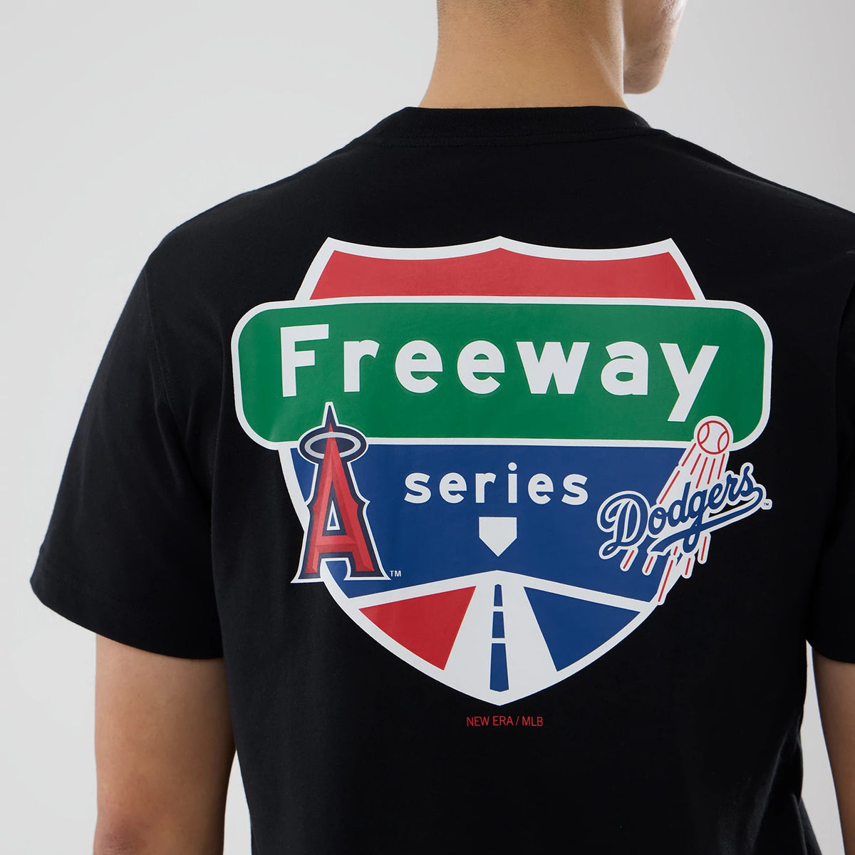 LA Angels MLB City Series Black T-Shirt, rear view showing a prominent freeway sign graphic in green, red, and blue with the Angels and Dodgers logos, printed on the centre back below a small New Era/MLB text.