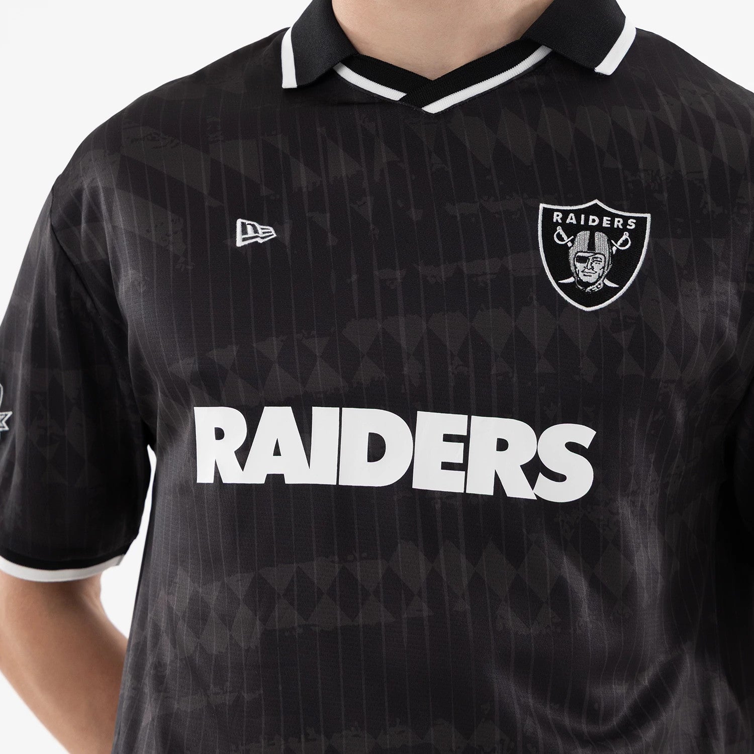 Las Vegas Raiders NFL Black Soccer Jersey, close-up on a model showing the white Raiders wordmark across the chest, embroidered team crest on the left side, and the New Era flag logo on the right.