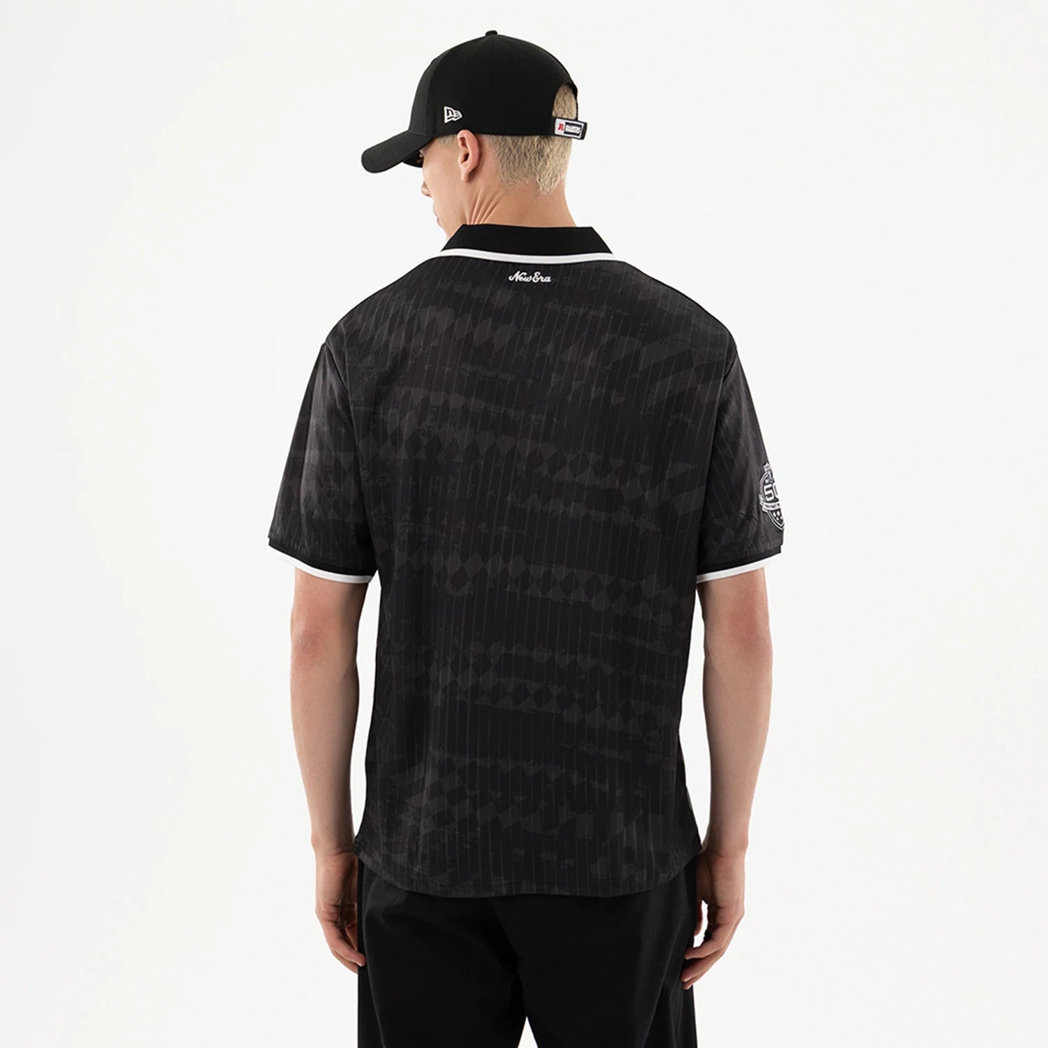 Las Vegas Raiders NFL Black Soccer Jersey, back view on a model wearing a black cap, featuring subtle tonal striping and a white embroidered logo on the right sleeve over white-trimmed black sleeves.