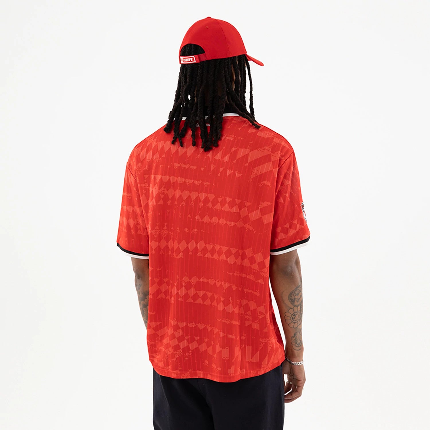 Kansas City Chiefs NFL Red Soccer Jersey, back view on a model with a red cap, showing a geometric pattern across the back, white and black trim on the collar and sleeves, and tattooed arms.
