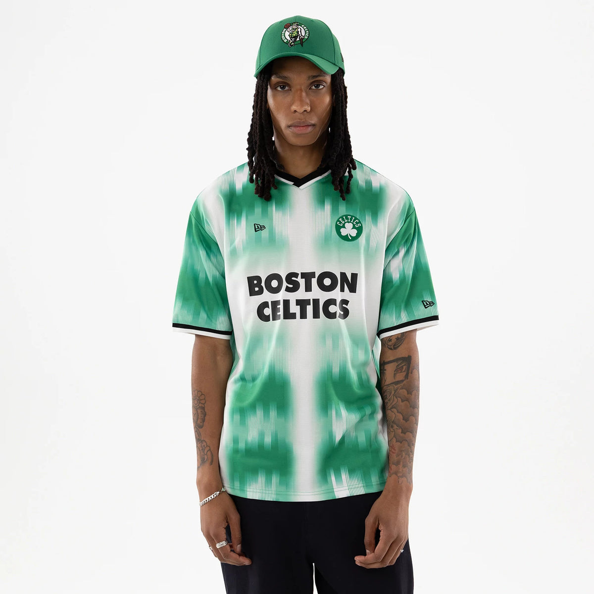 Boston Celtics NBA Green Soccer Jersey, front view on a model wearing a matching green cap, featuring bold black Boston Celtics lettering across the chest, a Celtics logo on the left chest, and New Era flag logos on the sleeves.