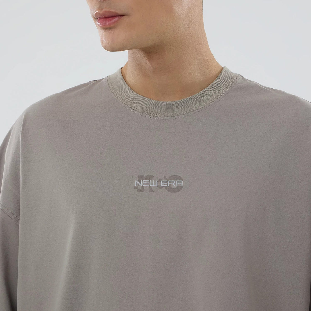 New Era NEC Logo Beige Oversized T-Shirt, front view showing the light beige fabric with a centred raised New Era logo in white on the chest, featuring a loose fit with a ribbed beige collar.