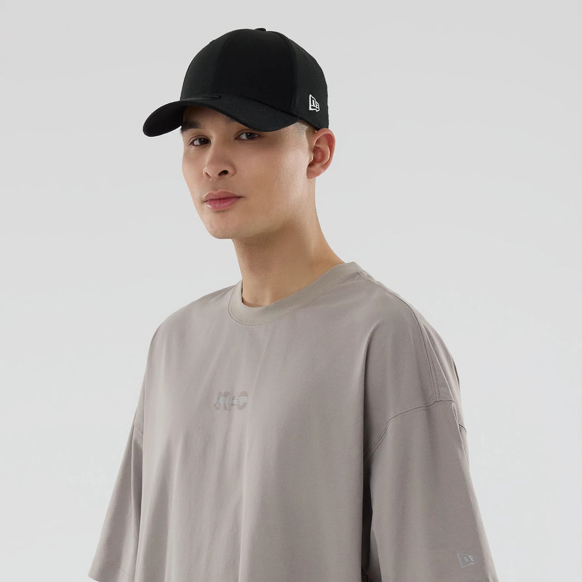 New Era NEC Logo Beige Oversized T-Shirt, on-model view showing the debossed NEC logo centred on the chest, a relaxed beige fit with short sleeves, and a debossed New Era logo on the left sleeve.