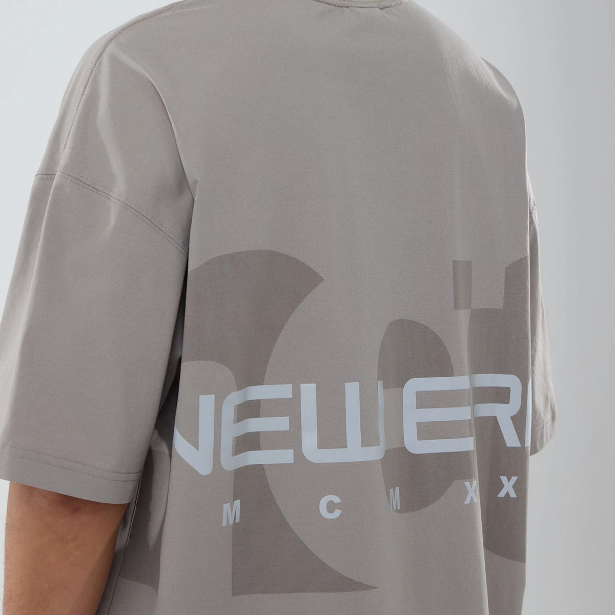 New Era NEC Logo Beige Oversized T-Shirt, rear view showing the printed New Era logo in white across the lower back against the beige fabric, with short sleeves and a relaxed fit design.