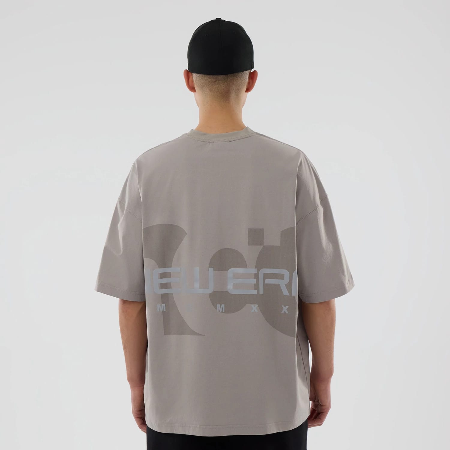 New Era NEC Logo Beige Oversized T-Shirt, rear view showing the large printed logo across the upper back of the neutral-coloured shirt worn by a person facing away, featuring short sleeves and a relaxed fit.