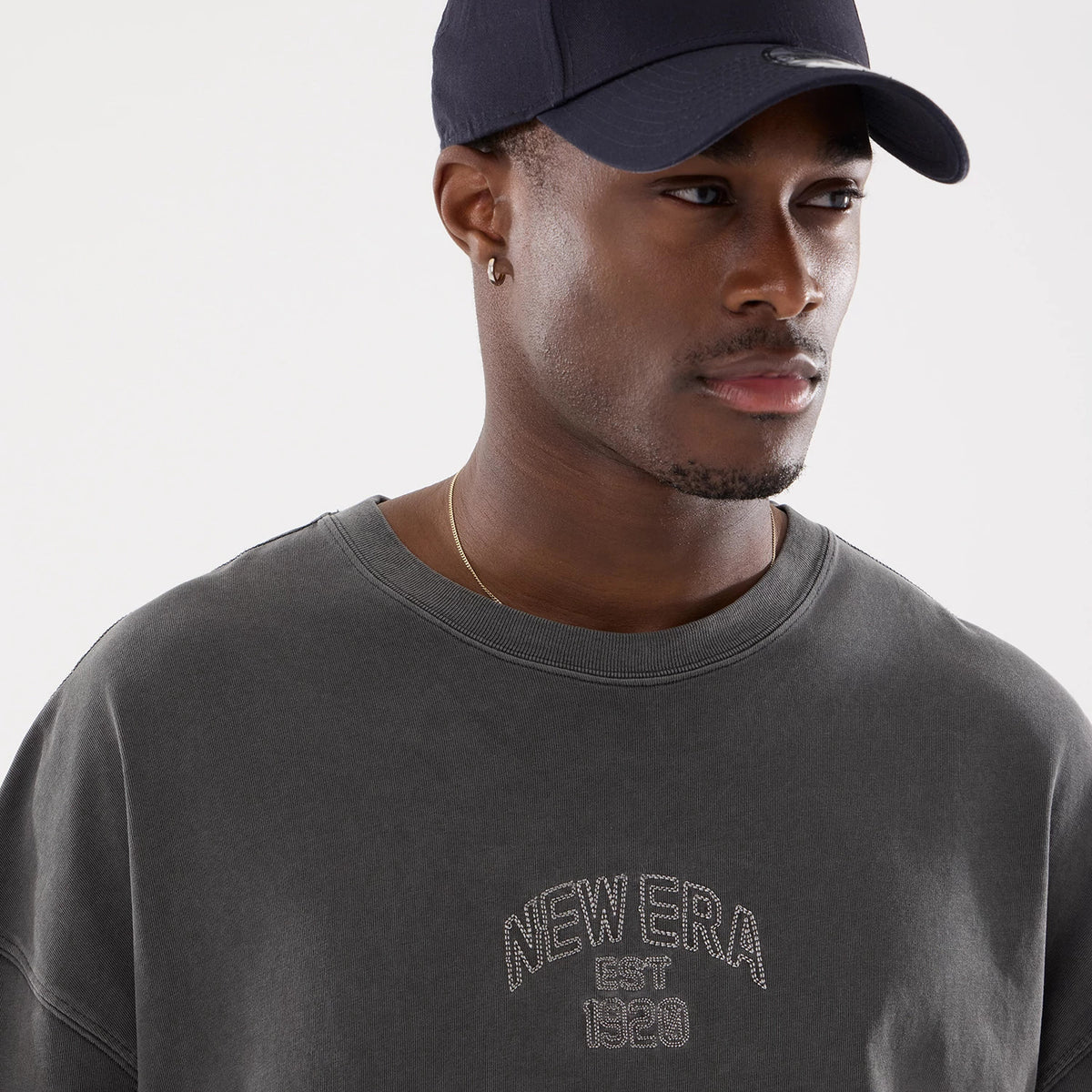 New Era Graphic Street Archived Washed Black Oversized T-Shirt, on-model view showing the grey oversized fit with a raised "NEW ERA EST 1920" logo centred on the chest, worn by a person in a dark cap.