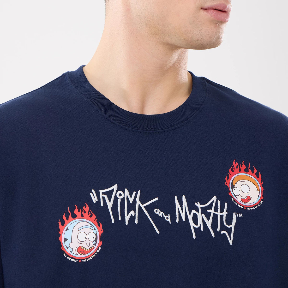New Era Rick And Morty Blue T-Shirt, front view showing the navy blue fabric with a white embroidered Rick and Morty logo on the chest flanked by cartoon character faces in flames on either side.