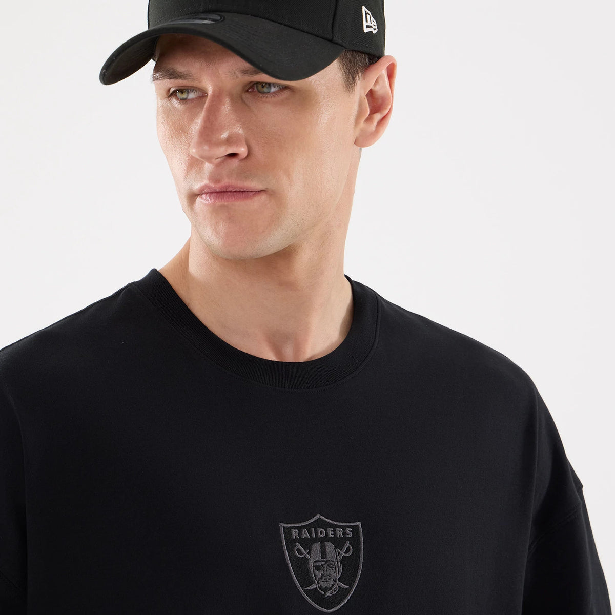 Las Vegas Raiders NFL Raiders Wear Black Oversized T-Shirt, front view showing a raised Raiders logo on the chest, paired with a black cap featuring a debossed New Era logo on the side.