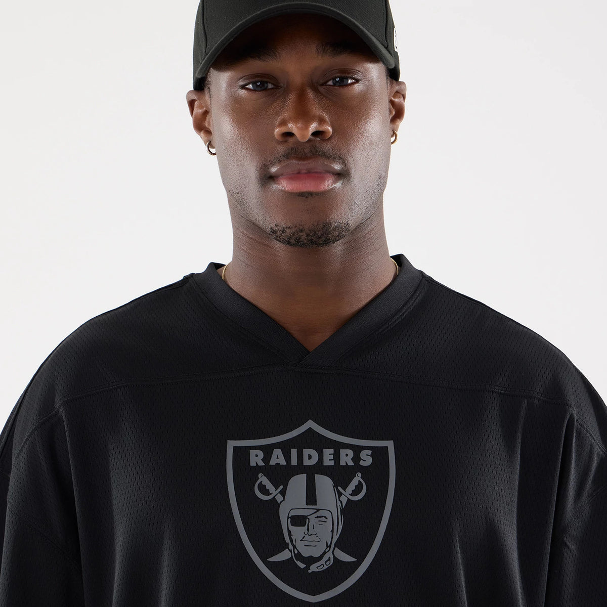 Las Vegas Raiders NFL Raiders Wear Black Mesh Oversized T-Shirt, front view showing a grey Raiders emblem centred on the chest, a textured v-neckline, and worn by a person with a black cap on their head.
