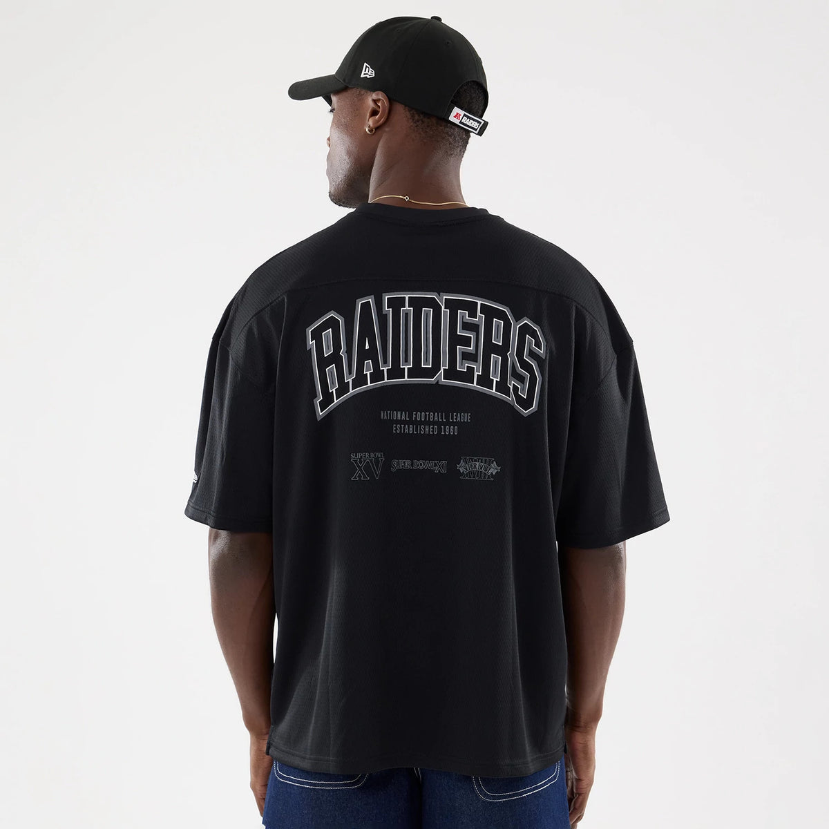Las Vegas Raiders NFL Raiders Wear Black Mesh Oversized T-Shirt, rear view showing large grey "RAIDERS" print across the upper back with smaller logos below on black mesh fabric, worn by a model in a black cap with a debossed side logo.