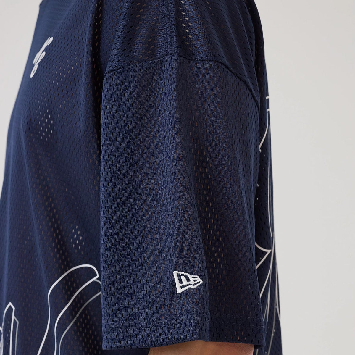 New Era Mix League Blue Oversized Mesh T-Shirt, side view showing the dark blue mesh fabric with a raised white New Era logo on the sleeve and abstract printed design elements extending from the front to the back.