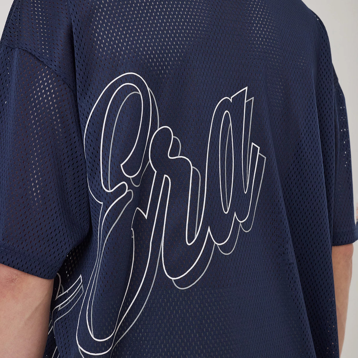 New Era Mix League Blue Oversized Mesh T-Shirt, side view showing the large script text across the back in white outline on navy mesh, emphasising the roomy fit and design of the oversized t-shirt.