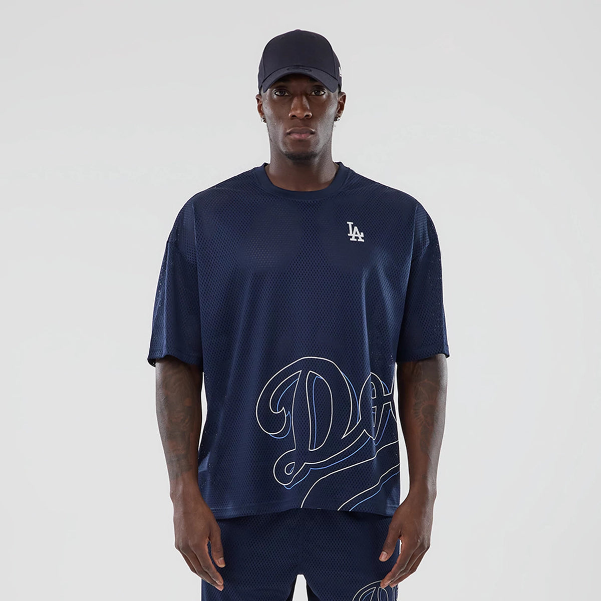 LA Dodgers MLB Mix League Blue Oversized Mesh T-Shirt, front view showing a dark blue mesh fabric with a small LA logo embroidered on the chest, paired with matching shorts and a dark cap, with large white 'Dodgers' script across the lower half.