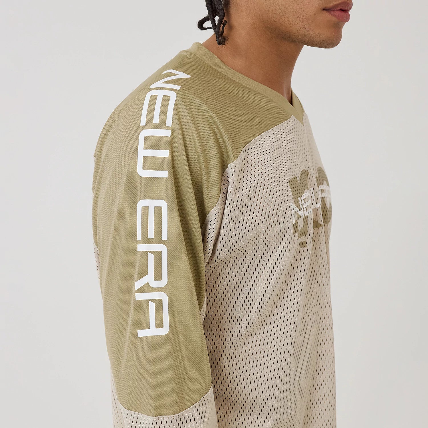 New Era NEC Logo Beige Long Sleeve Jersey, side view on a model showing the white New Era text on the olive left sleeve and matching logo on the chest, with a breathable perforated fabric design.