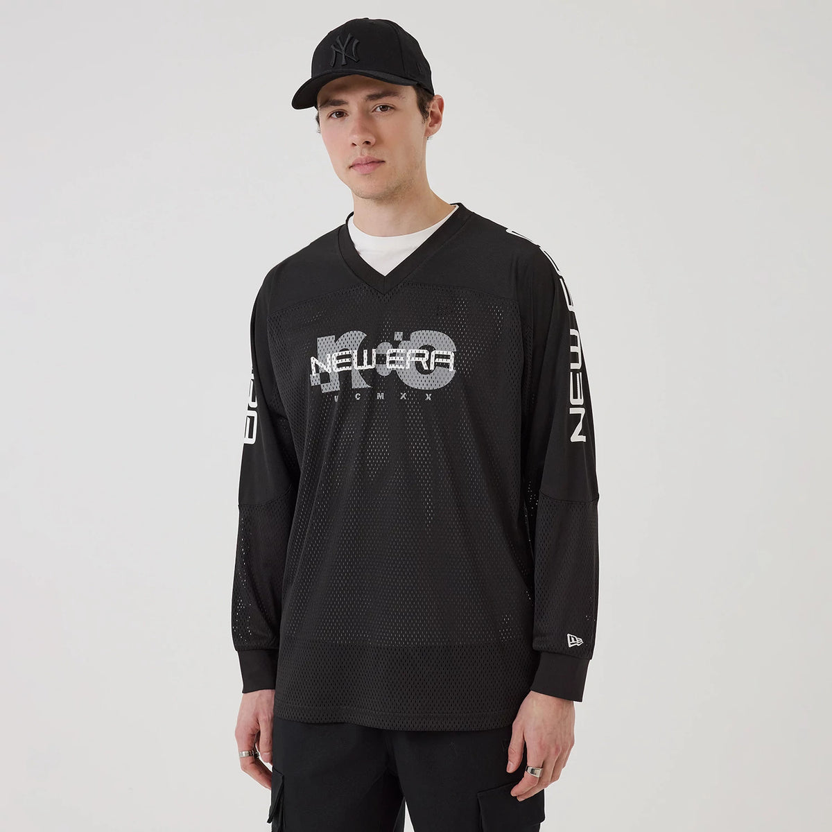 New Era NEC Logo Black Long Sleeve Jersey, front view on a model wearing a black cap, showcasing the white New Era logo centred on the chest with mesh fabric and additional branding on the sleeves.
