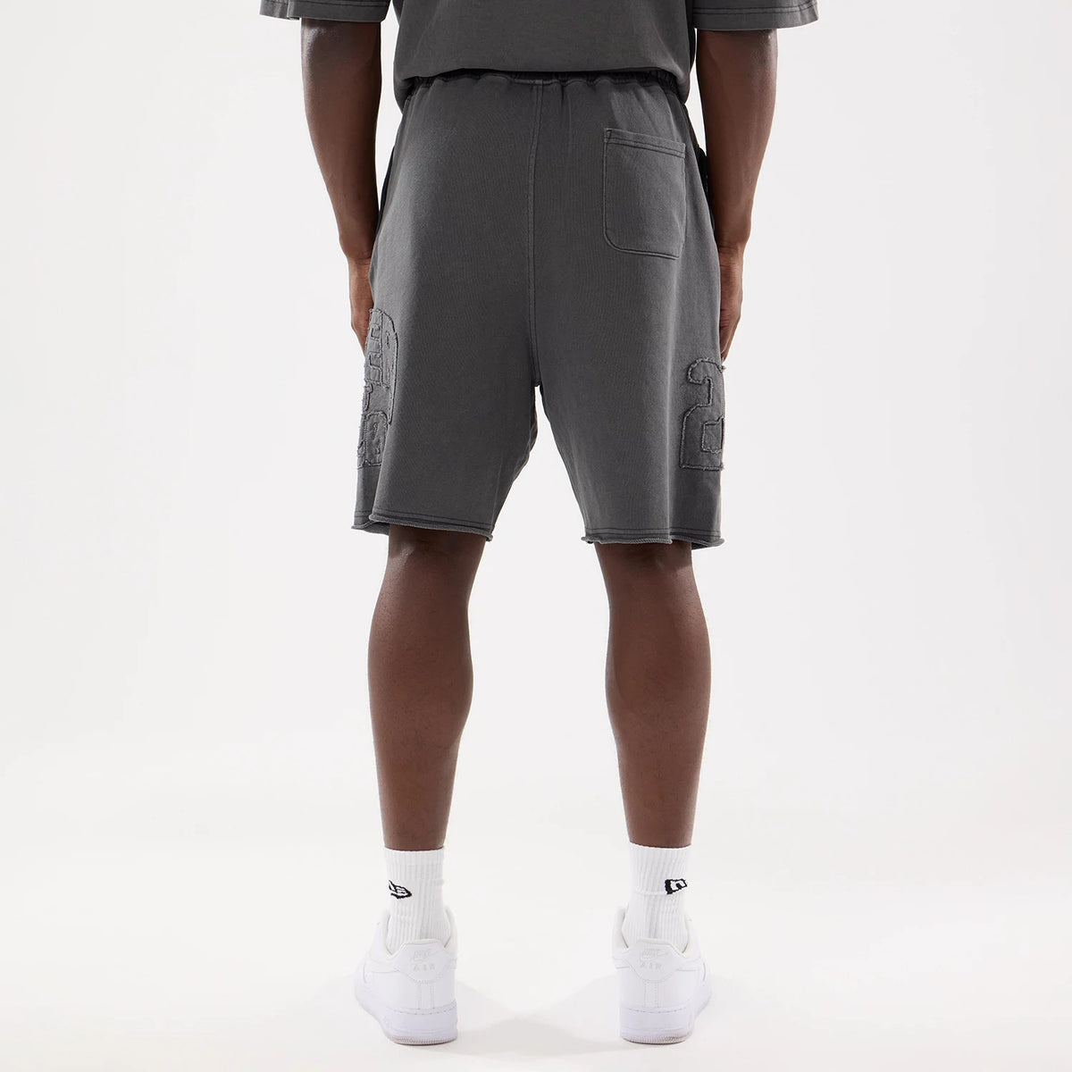 New Era Street Archived Black Oversized Shorts, rear view showing the dark grey colour, elasticated waistband, a single patch pocket on the right side at the back, and raised embroidered numbers on the lower side of each leg.