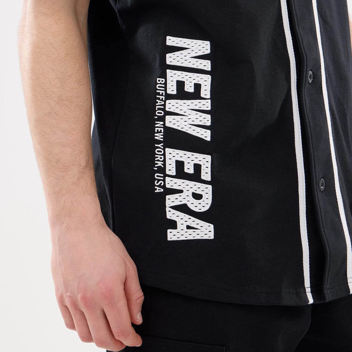 New Era Basic Black Jersey, side view showing the white embroidered New Era logo with "Buffalo, New York, USA" lettering vertically on the lower left side, featuring white piping along the button closure.