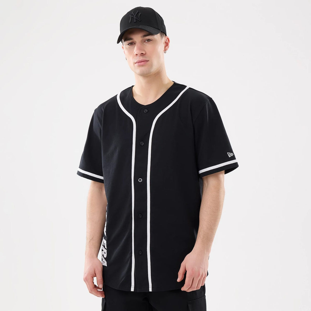 New Era Basic Black Jersey, on-model front view with white piping along the edges and sleeves, featuring button closure, New Era script on the side, and a New Era flag logo on the left sleeve, paired with a matching cap.