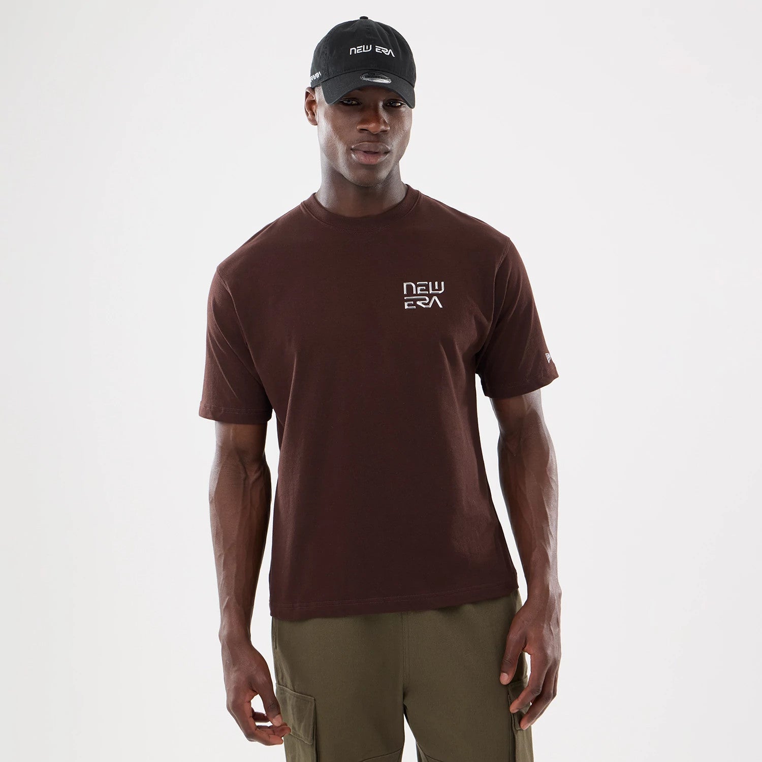 San Diego Padres Hajime Sorayama X MLB Dark Brown T-Shirt, on-model view showing the dark brown t-shirt with a raised New Era logo on the left chest, short sleeves, and a black cap with the New Era logo worn by the model.