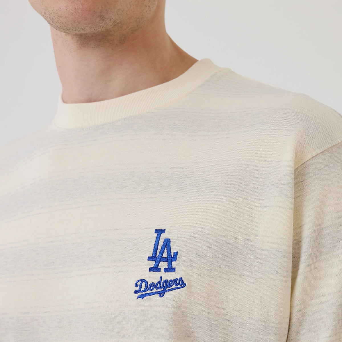 LA Dodgers MLB Border Cream Oversized T-Shirt, front view showing a cream shirt with light horizontal stripes and a blue embroidered LA Dodgers logo on the left chest, featuring a ribbed neckline.