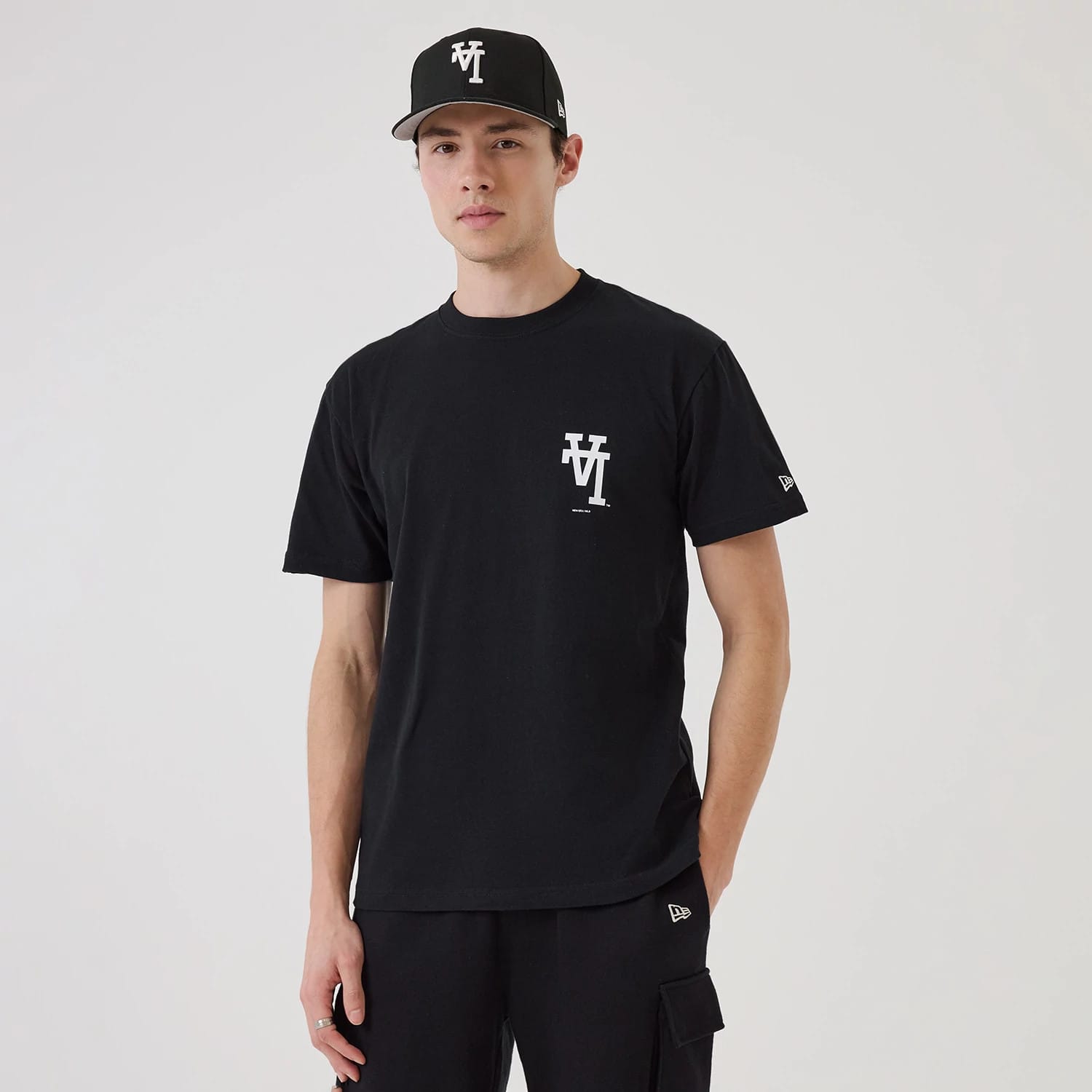 LA Dodgers MLB Upside Down Black T-Shirt, on-model view showing the white logo printed on the left chest, short sleeves with the New Era patch on the left sleeve, paired with a black cap featuring a white raised logo on the front.
