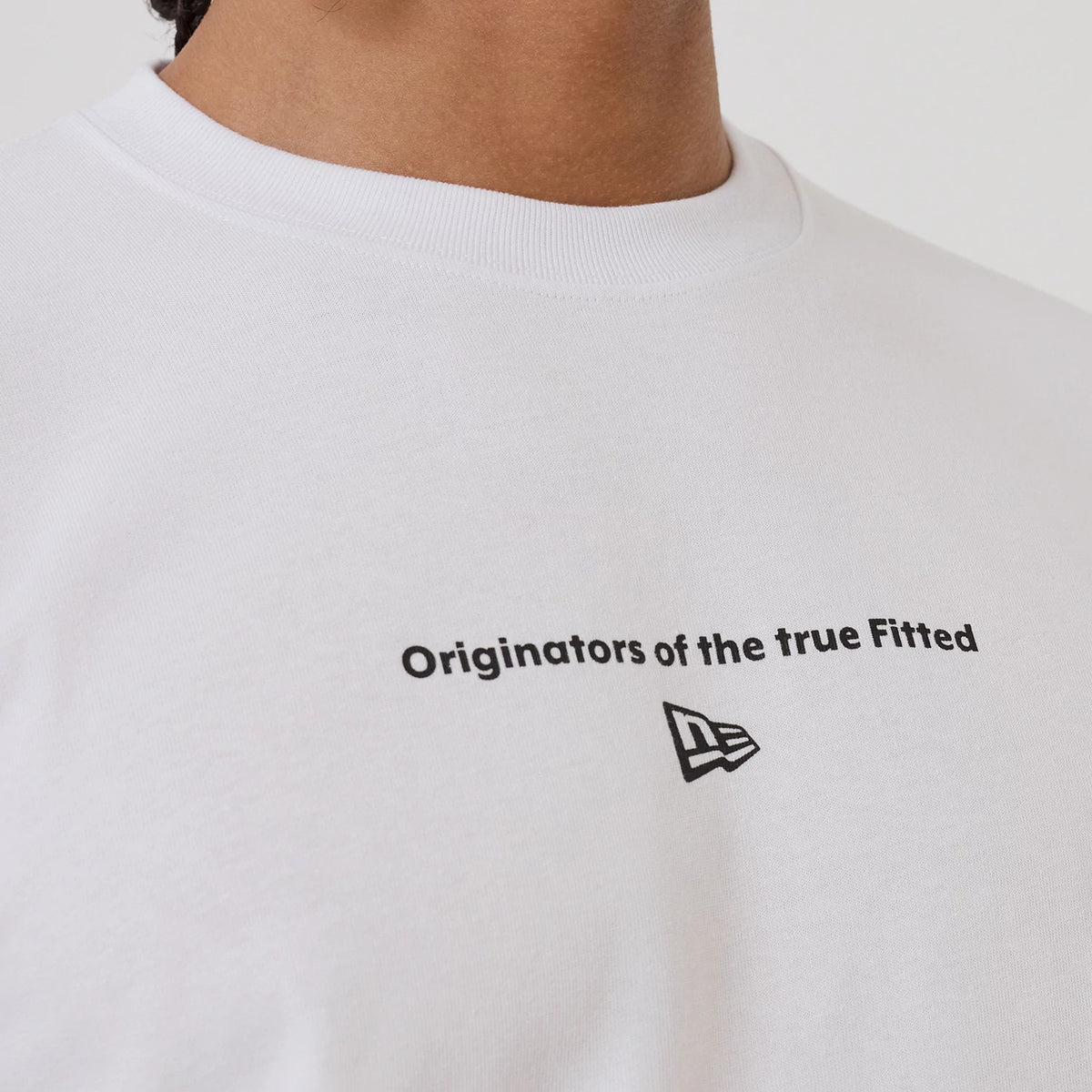 New Era Circle White T-Shirt, front view showing a black lettered slogan "Originators of the true Fitted" across the chest and an embossed New Era logo positioned below the text on the plain white fabric.