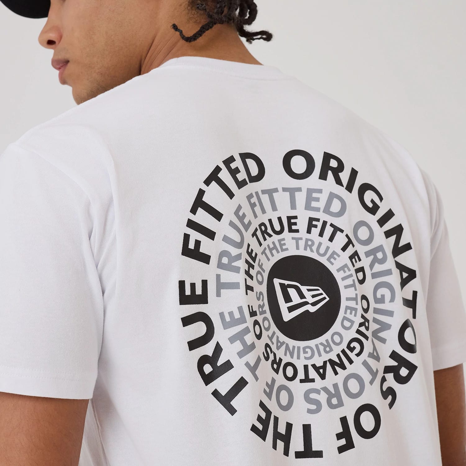 New Era Circle White T-Shirt, on-model view showing the back of the white T-shirt with a large circular black and grey graphic featuring a raised New Era logo at the centre, worn by a person with a black cap.