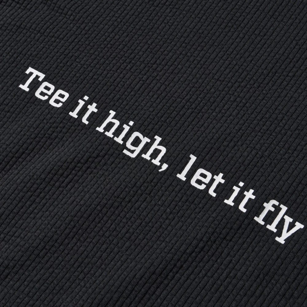New Era Seersucker Black Polo T-Shirt, close-up view featuring the textured black fabric with the phrase Tee it high, let it fly printed in white letters across the fabric surface.