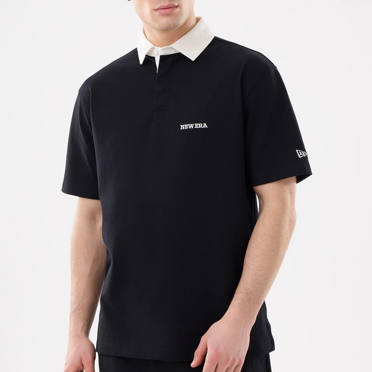 New Era Black Short Sleeve Rugby Shirt, front view on a model featuring a white contrasting collar, embroidered New Era lettering on the chest, and the New Era flag logo on the left sleeve.